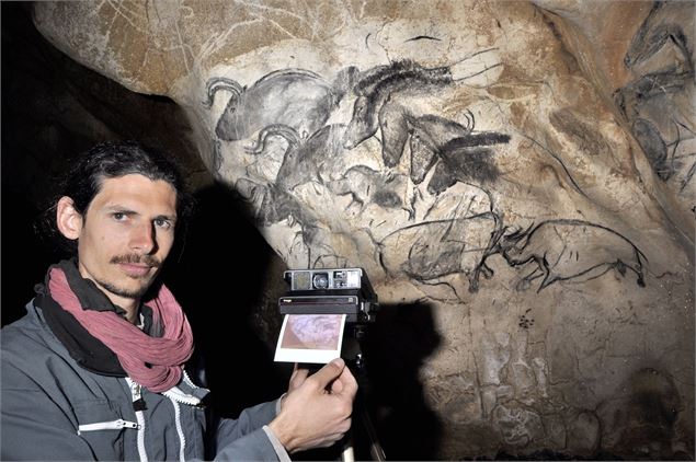 un homme prend une photo d'une peinture murale dans une grotte - J.-M. Geneste, Ministère de la Cult