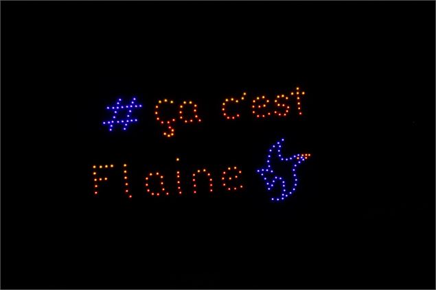 Spectacle de drones lumineux dans un ciel nocturne totalement noir. Les points de lumière forment le