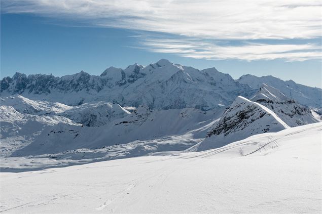 Le sommet enneigé du Mont-Blanc domine l'horizon au centre d'un vaste panorama alpin sous un ciel bl