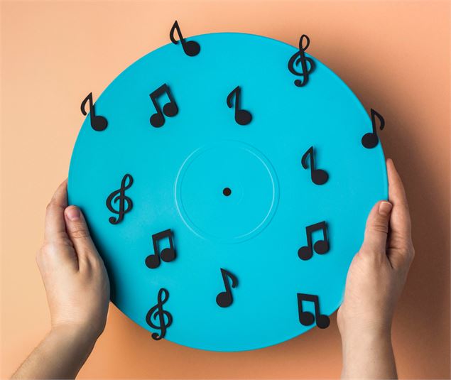 Des symboles musicaux sur un disque bleu, tenu par des mains - Carol Yepes / Freepik