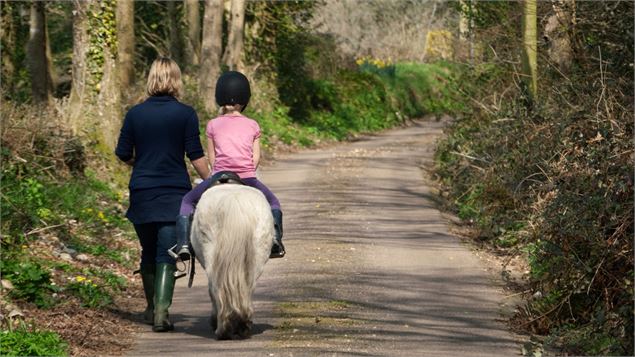 petite fille sur un poney avec une accompagnatrice - canva