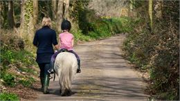 petite fille sur un poney avec une accompagnatrice - canva