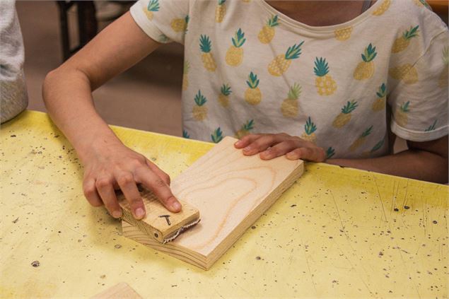 Enfant qui ponce sa planche en bois - Office de Tourisme Thônes Coeur des Vallées