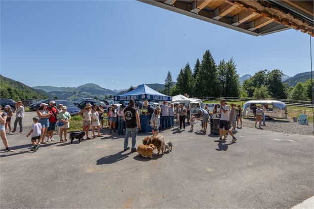 Sur une place, une petite foule discute et flâne autour d'un stand buvette. Présence de chiens tenus