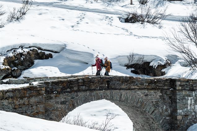Randonneur hivernal sur un pont en pierre menant au hameau de l'Ecot - M Challe