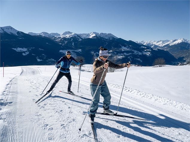 Couple de fondeurs sur une piste enneigée avec vue dégagée sur une chaine de montagne. - Tristan Shu