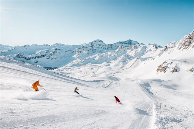 Des skieurs et snowboardeurs dévalent la piste rouge Cyclamen avec vue sur la Grande Motte - andypar