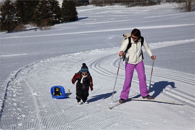 Enfant avec luge et sa maman en ski de fond sur le Plateau des Mouilles - Gilles Place / OT ADL