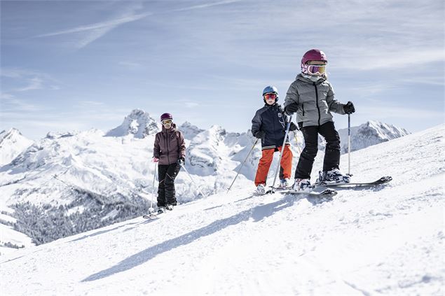 Famille de skieurs sur le domaine de ski alpin du Grand-Bornand, vue sur la chaîne des Aravis - T.Sh