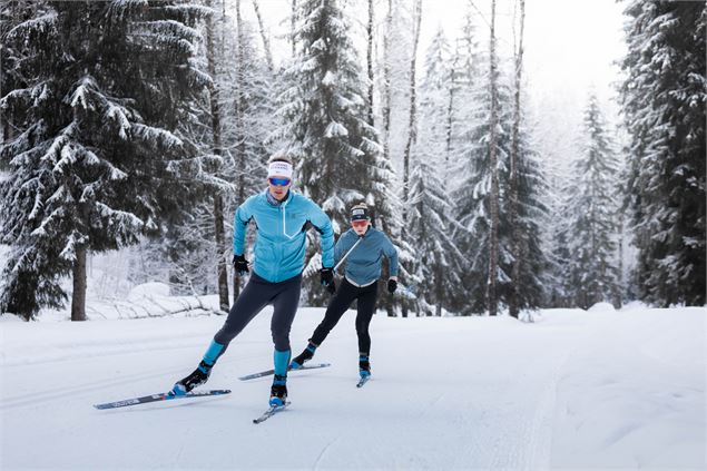 Deux skieurs sur une piste de ski nordique à travers les sapins au Grand-Bornand - C. Hudry