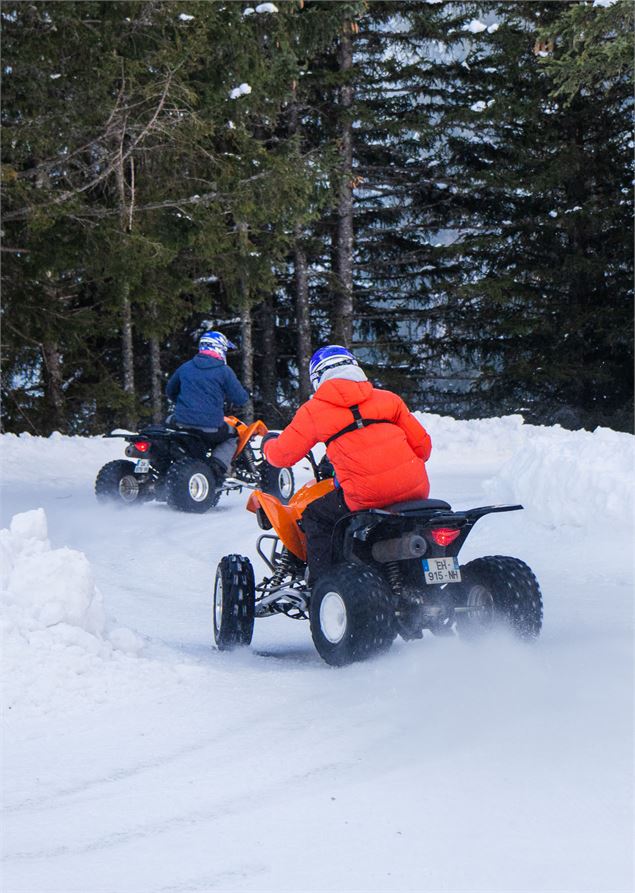 Deux personnes portant des casques et des vêtements d'hiver colorés pilotent des quads orange sur un