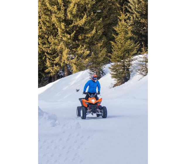 Une personne portant une veste bleue et un casque orange conduit un quad orange et noir sur un chemi