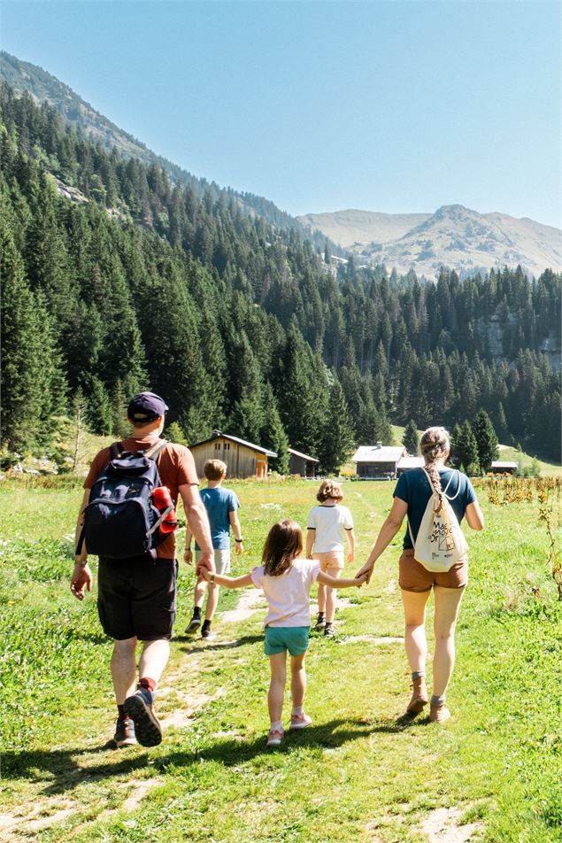 Une famille de dos randonne sur un sentier en herbe vers des chalets - OT Flaine-Candice Genard
